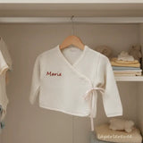 La brassière "Petit Câlin" dans sa nuance Sablé (beige clair) est la pièce parfaite pour un trousseau de naissance unisexe ou pour les parents qui préfèrent les tons naturels. 