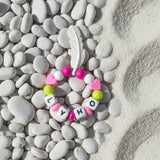 Anneau de dentition Lyho en silicone assorti aux couleurs anis et fushia avec plume blanche de 6 cm.