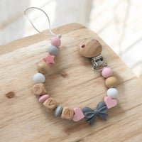 Attache tétine artisanale avec perles en silicone gris et bois naturel ornée d'un petit noeud gris pour bébé.