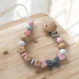 Attache tétine artisanale avec perles en silicone gris et bois naturel ornée d'un petit noeud gris pour bébé.