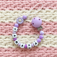 attache tetine silicone lilas marbré poser sur un fond de laine 