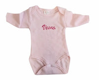 Body de naissance rose pour bébé fille avec finitions délicates posé à plat.