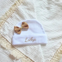 ce bonnet bébé naissance en coton blanc avec noeud couleur caramel poser à plat sur une tissus gaze de coton