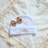 ce bonnet bébé naissance en coton blanc avec noeud couleur caramel poser à plat sur une tissus gaze de coton