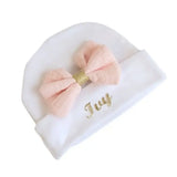bonnet bébé naissance en coton blanc avec noeud couleur rose pale personnalisé au prénom de bébé posé a plat 