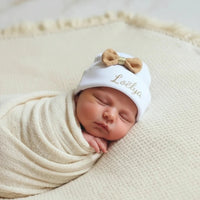 ce  bonnet bébé naissance blanc en coton personnalisé avec prénom avec son noeud en gaz de coton caramel 