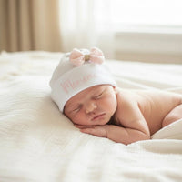 ce bonnet bébé naissance porter par un bébé de couleur blanc en coton personnalisé avec noeud rose en gaz de coton