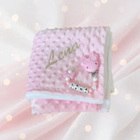 ce coffret cadeau naissance fille se compose d'un plaid rose et d'une attache tetine mam tout deux personnalisé au prénom de bébé .
