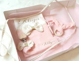 présentation d'un coffret cadeau naissance personnalisée de couleur rose avec une attache tétine une housse de carnet de santé un anneau de dentition et une boite cadeau personnalisée