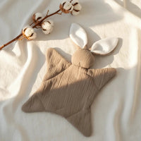 doudou sans yeux marron en gaze de coton poser a plat sur une couverture 