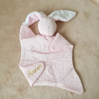 doudou sans yeux rose pale en gaze de coton poser a plat sur une couverture avec le prénom de bébé 