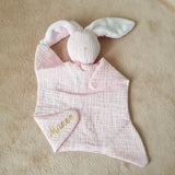doudou sans yeux rose pale en gaze de coton poser a plat sur une couverture avec le prénom de bébé 
