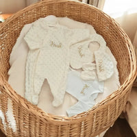 grenouillère bébé fille poser a plat avec son bonnet ses moufles son body et bavoirs assortis dans un panier osier