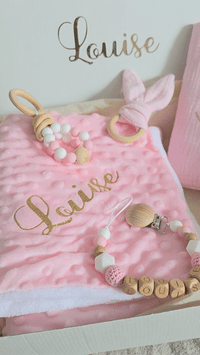présentation en vidéo d'un coffret naissance fille personnalisé avec une attache tetine, un protège carnet de santé
 un anneau de dentition, u, hochet oreille de lapin et une couverture plaide naissance.