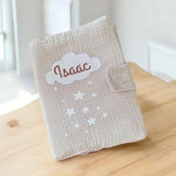 Vue rapprochée d'un protège carnet de santé en gaze de coton beige motif nuage étoilé avec personnalisation par flocage du prénom